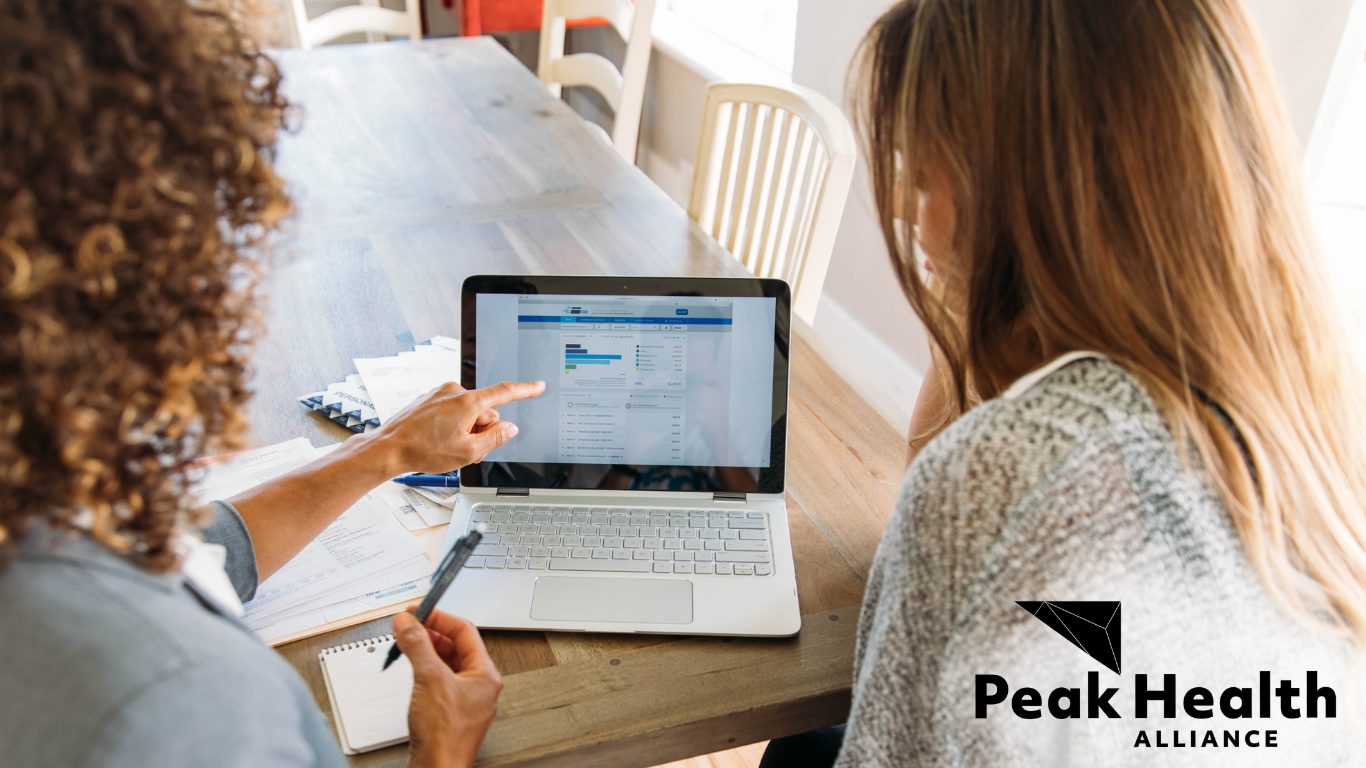 Two women looking at a laptop computer together. The Peak Health Alliance logo is in the lower right-hand corner.